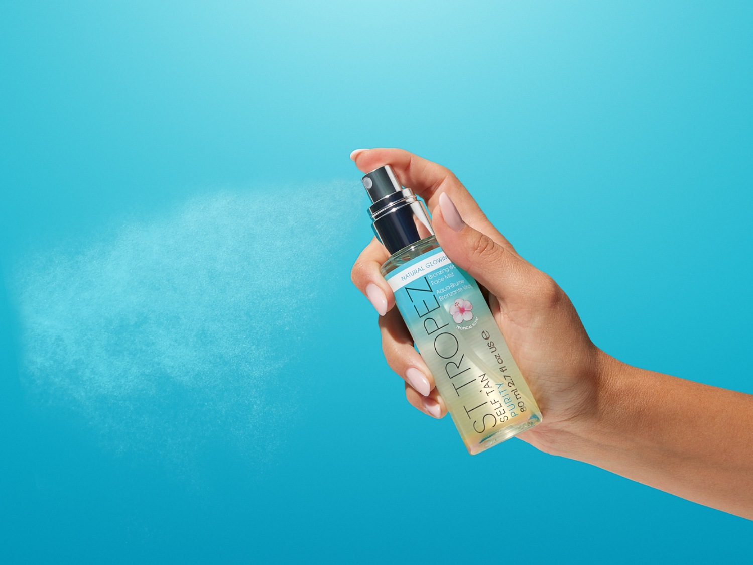 A képen egy kéz látható, amint a St. Tropez önbarnító arcpermetet használja, melynek átlátszó flakonján a termék neve és leírása olvasható.