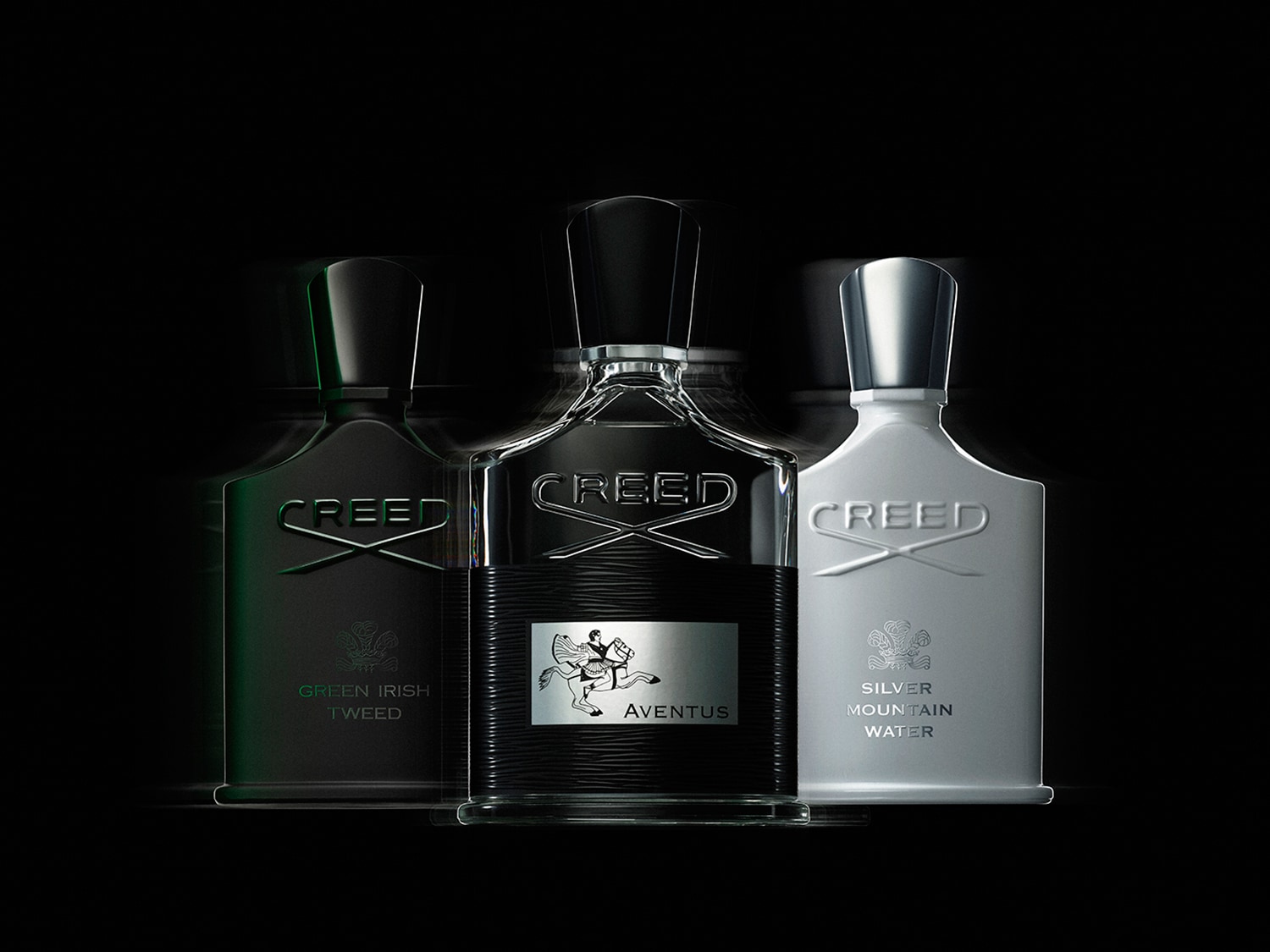 Trzy flakony perfum Creed w odcieniach zieleni, czerni i bieli, elegancko prezentujące zapachy Green Irish Tweed, Aventus i Silver Mountain Water.