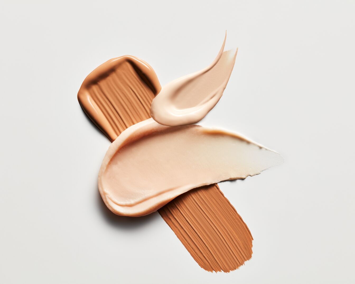 Na białym tle widoczne są próbki podkładu w różnych odcieniach beżu i brązu, tworzące abstrakcyjny wzór.