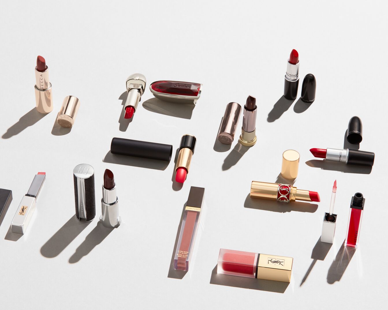 Różnorodność pomadek do ust w odcieniach czerwieni, różu i brązu, w eleganckich opakowaniach marek takich jak YSL, MAC i Givenchy, idealnych do makijażu.