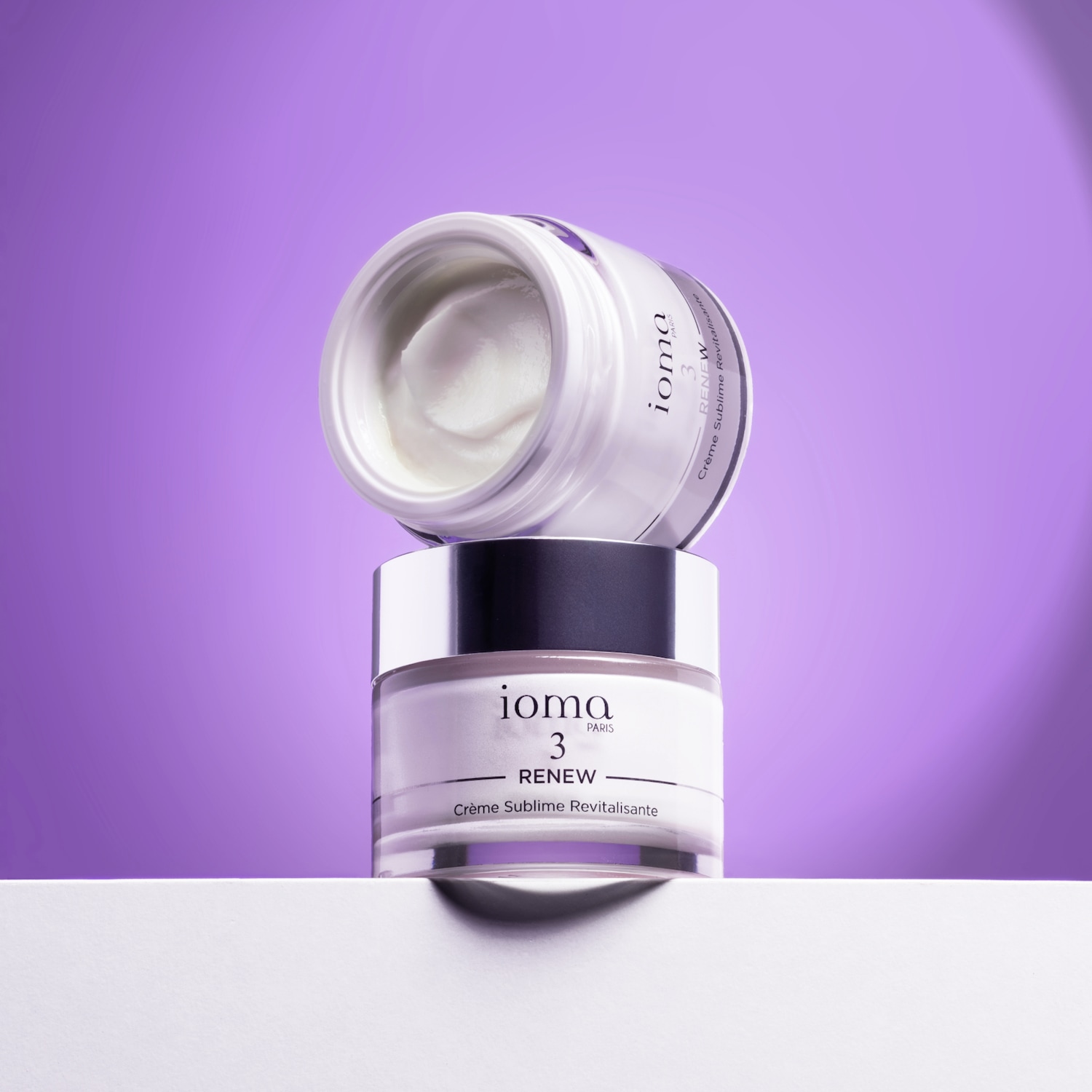Ecco Ioma Paris 3 Renew Crème Sublime Revitalisante, un duo di lussuose creme in vasi bianchi impilati su uno sfondo viola.
