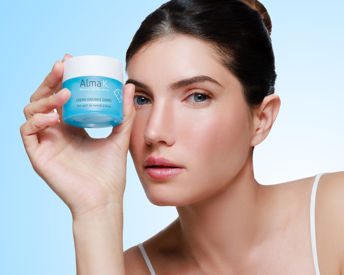 Una donna tiene in mano un vasetto di crema idratante Alma K. con confezione azzurra e bianca, ideale per pelli normali e miste, per una cura quotidiana.