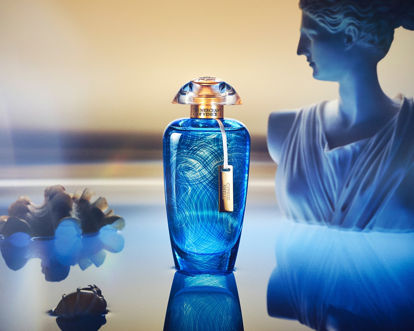 Błękitny flakon perfum The Merchant of Venice Cyprus Shell z przezroczystą nakrętką i złotą zawieszką na tle rzeźby kobiety.