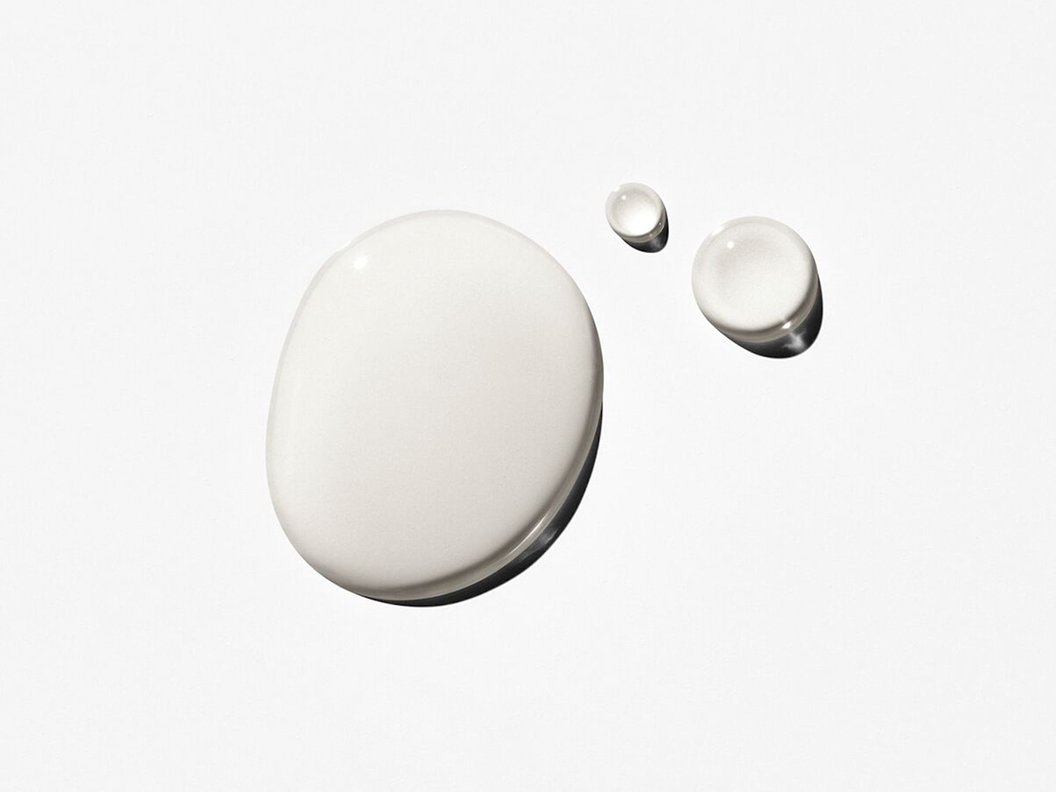 Gocce di siero bianco latte su una superficie chiara, che mostrano la consistenza liscia e idratante del prodotto.