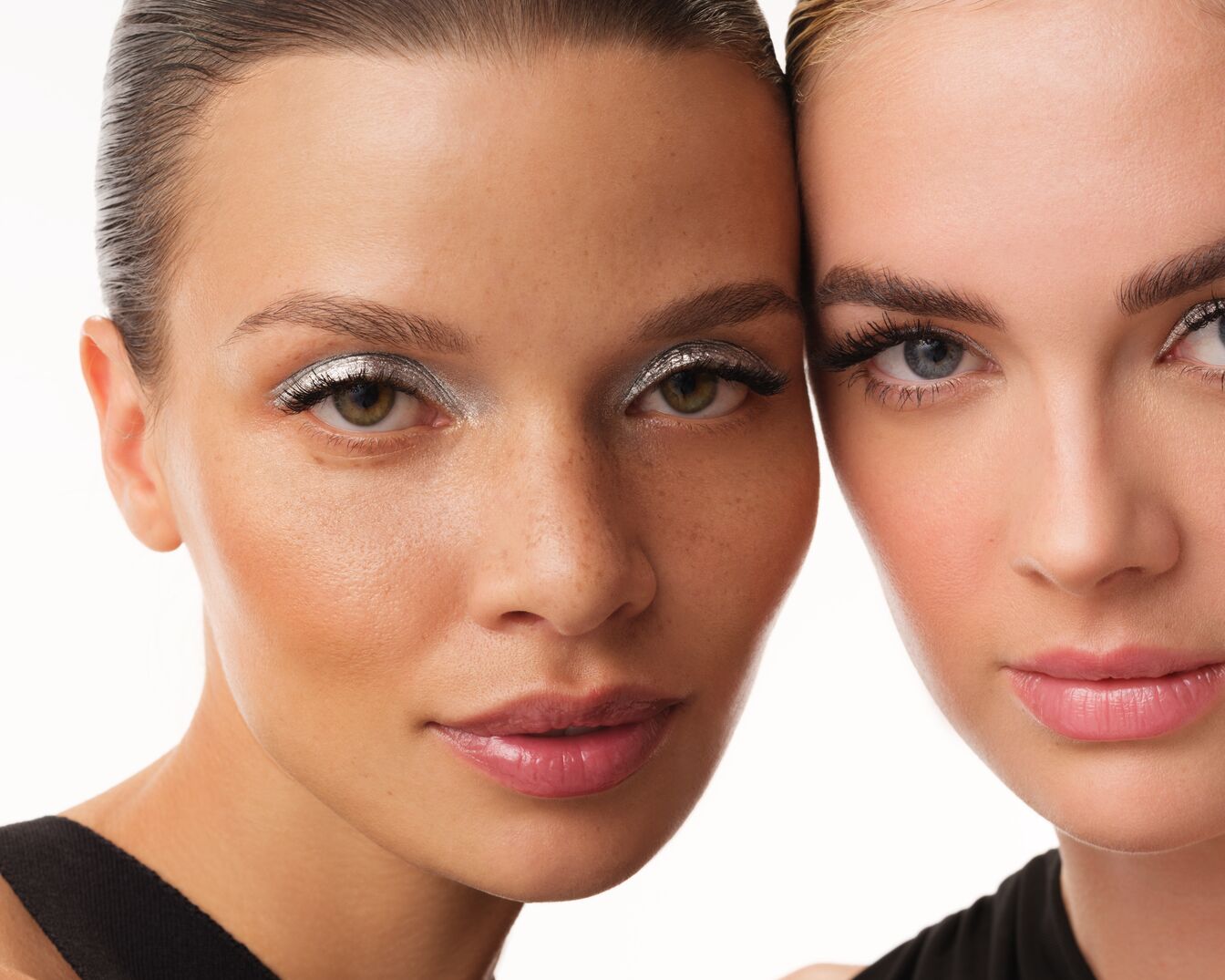 Primo piano di due donne con ombretto argentato scintillante, incarnati diversi e labbra lucide, che mostrano un look moderno e luminoso.