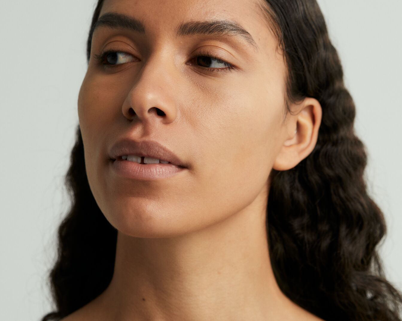 Primo piano di una donna con pelle liscia e capelli scuri ondulati, che mostra un incarnato uniforme e un aspetto naturale.