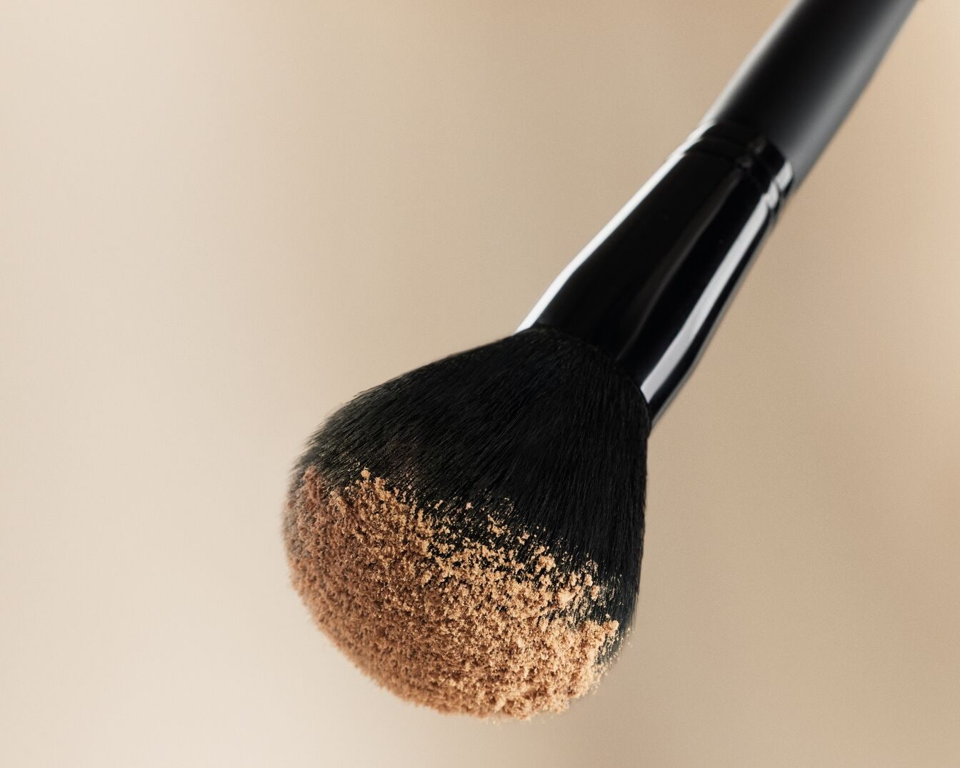 Ecco un pennello da trucco con setole nere e polvere color carne, ideale per applicare il fondotinta in modo uniforme.