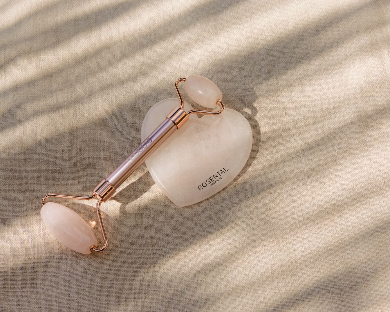 Rullo di giada rosa con manico color oro rosa, appoggiato su una pietra di giada bianca a forma di cuore, per un massaggio rilassante e rivitalizzante.