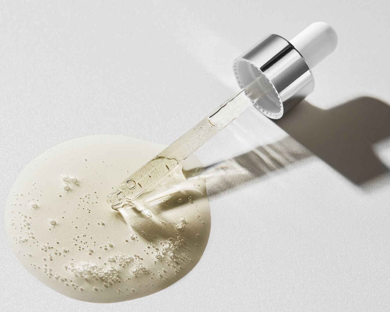 Gros plan sur un homme appliquant un sérum transparent sur sa peau à l'aide d'une pipette en verre, mettant en valeur l'hydratation et les soins de la peau.