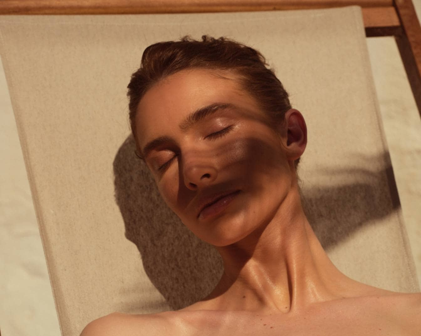 Una donna con gli occhi chiusi si rilassa su una sedia a sdraio, godendosi il sole caldo sulla sua pelle luminosa.