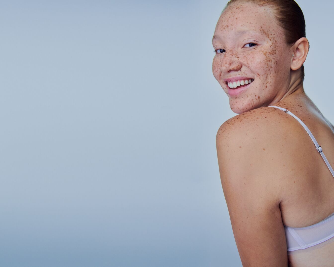 Gros plan sur le visage d'une femme avec les yeux fermés et une crème blanche appliquée, mettant en valeur une peau hydratée et un teint uniforme.