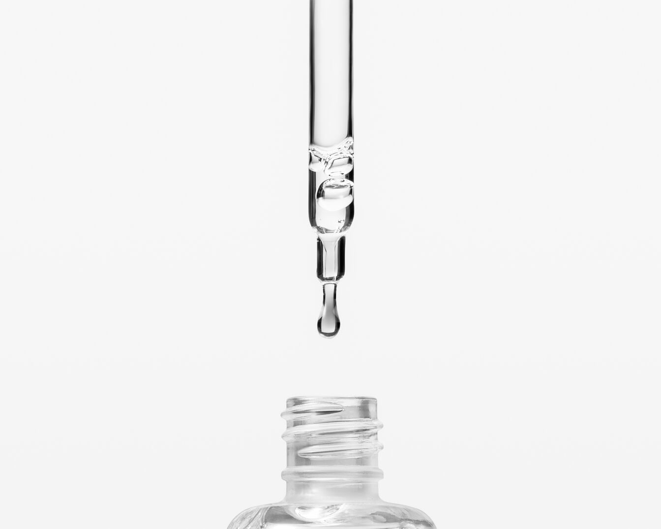 Klarer Tropfen Serum fällt aus einer Pipette in eine durchsichtige Flasche, bereit für die Anwendung für strahlende Haut.