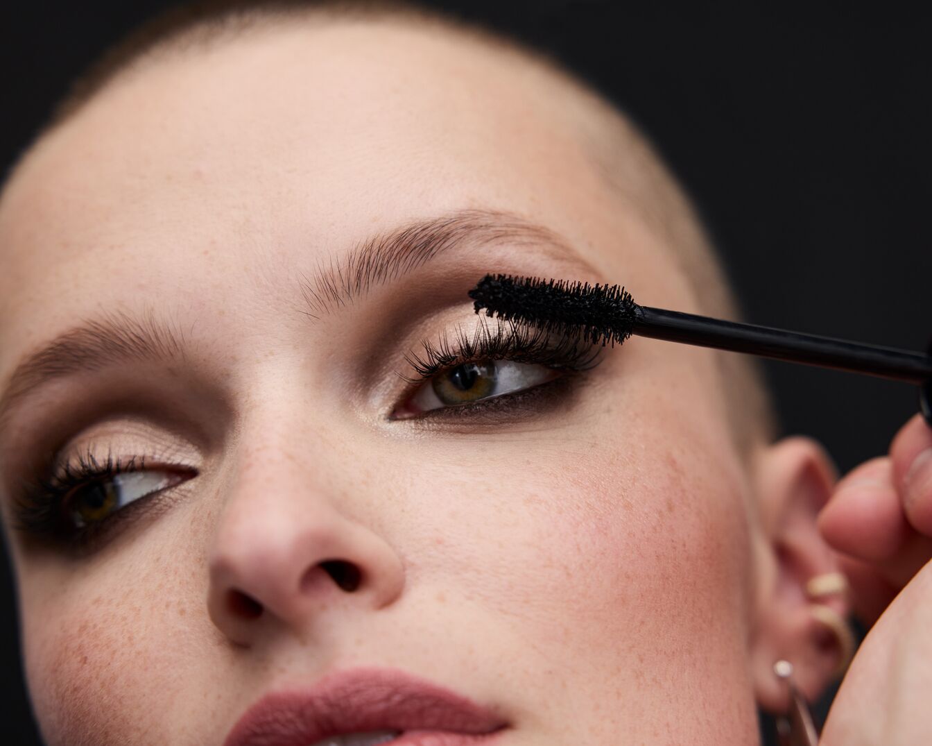 Primo piano di una donna che applica il mascara nero sulle ciglia superiori per allungarle e dare volume, completando il suo look.