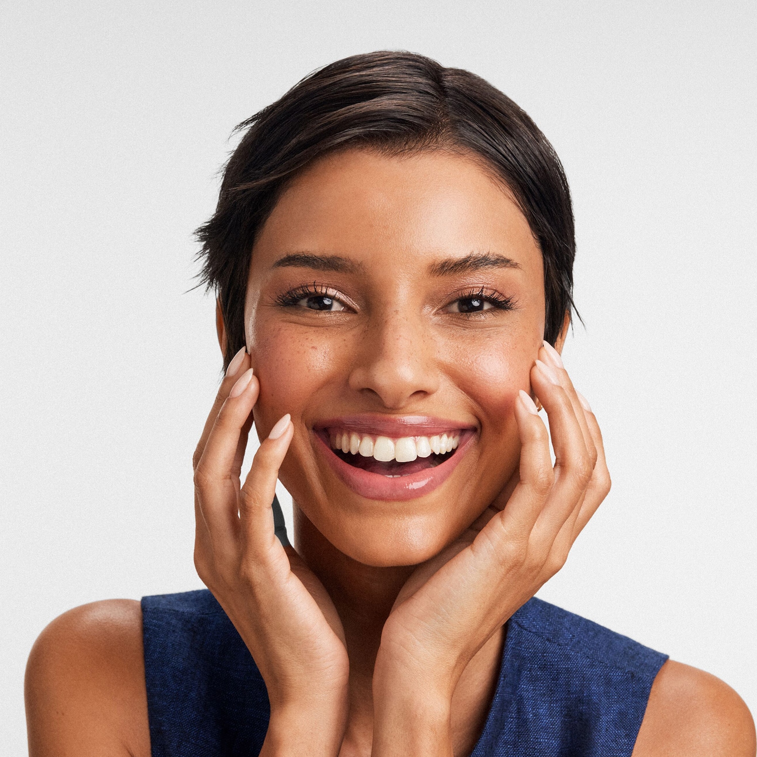 Une femme souriante, les mains sur les joues, rayonne de bonheur et de confiance.