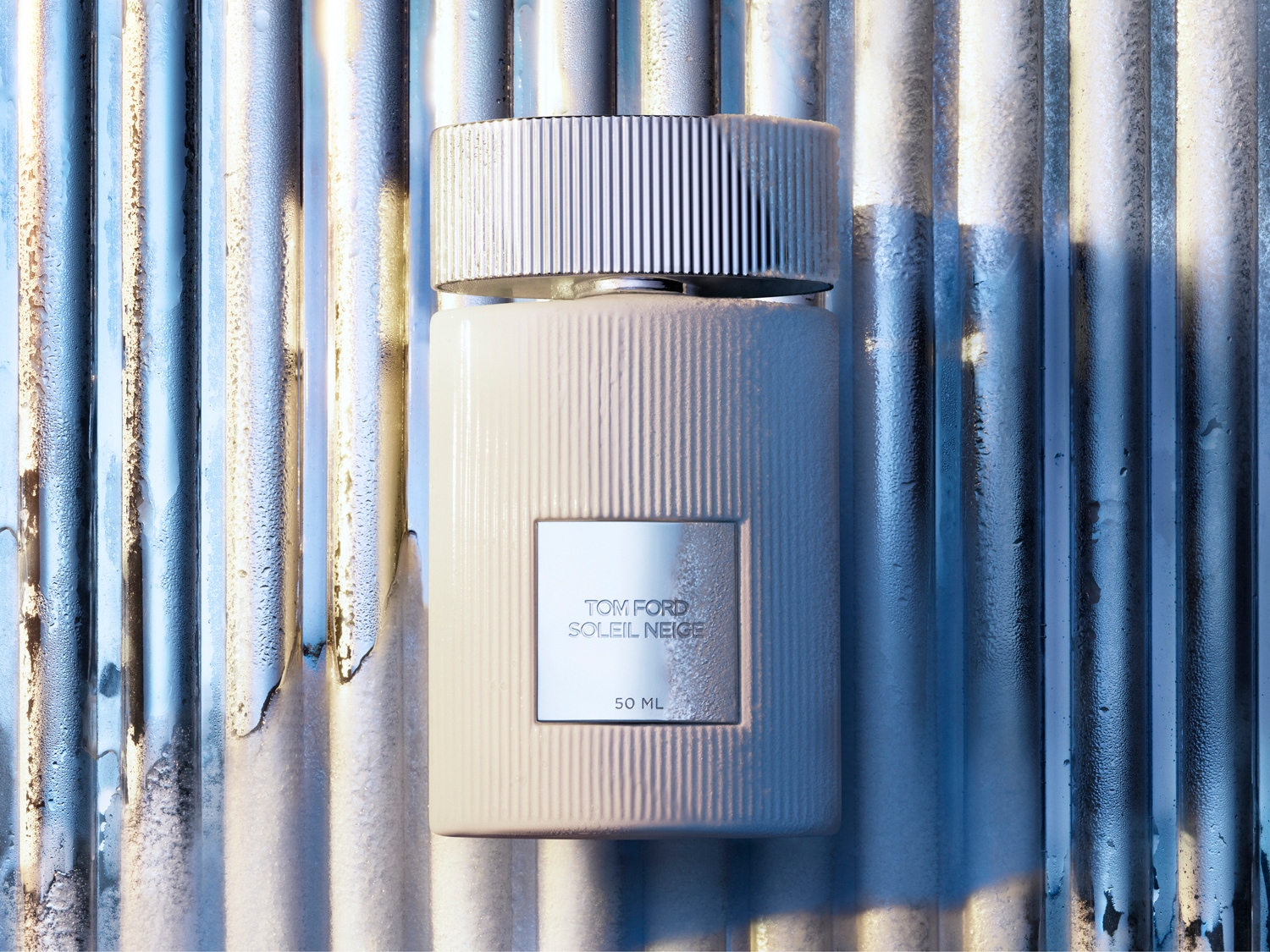 El frasco de perfume Tom Ford Soleil Neige de 50 ml, con su diseño acanalado en blanco y tapón plateado, evoca la elegancia y el lujo.