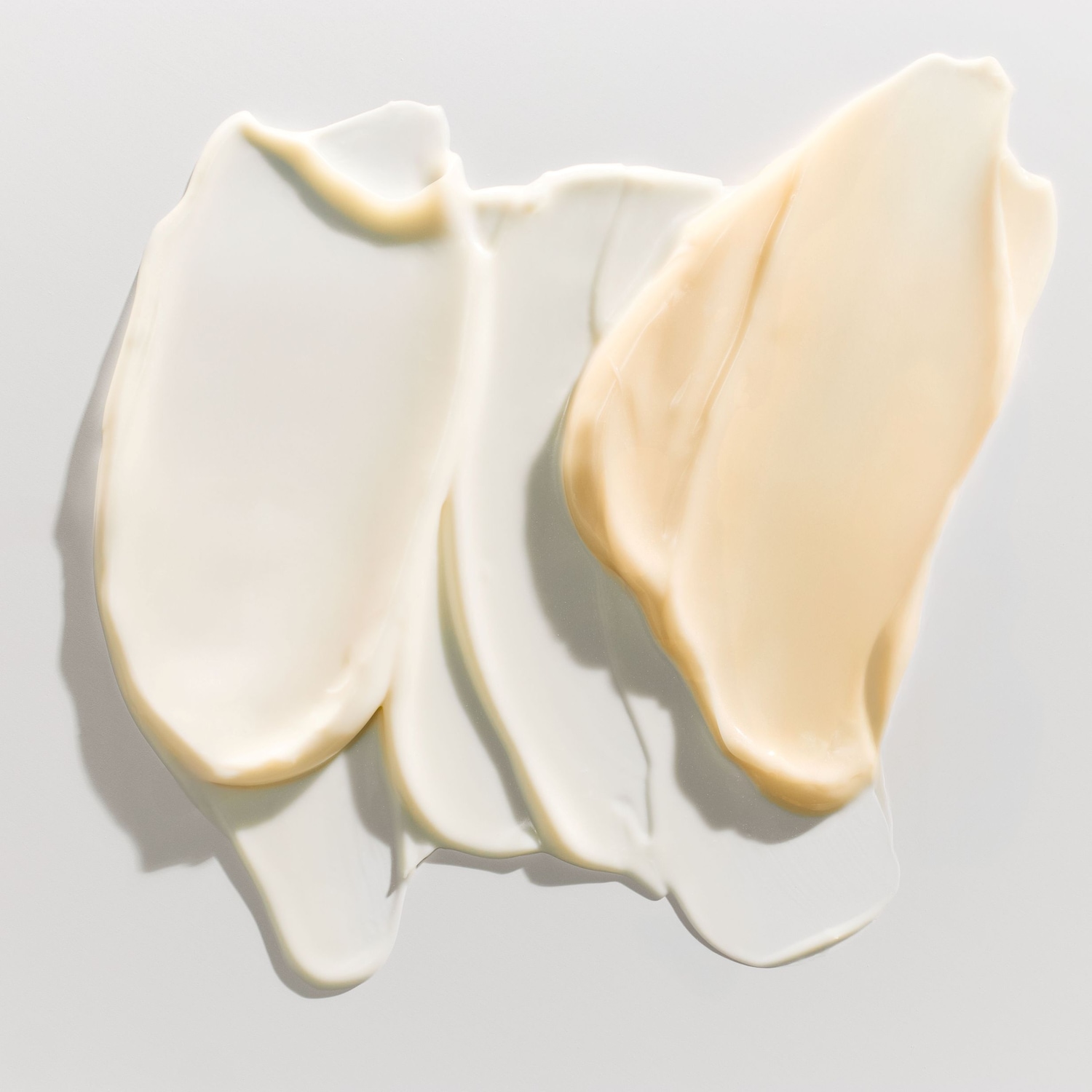 Primo piano di campioni di crema idratante in diverse tonalità di bianco e beige, che mostrano la consistenza liscia e ricca del prodotto.