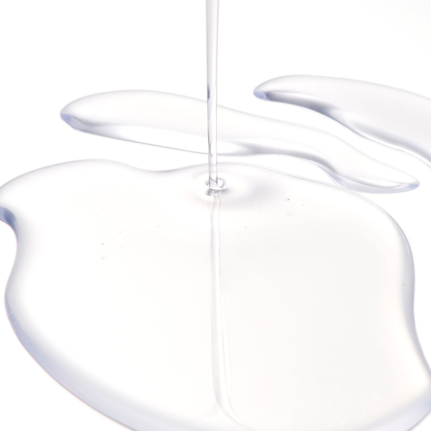 Versamento di liquido trasparente, che crea una pozza lucida su una superficie bianca, suggerendo purezza e idratazione.