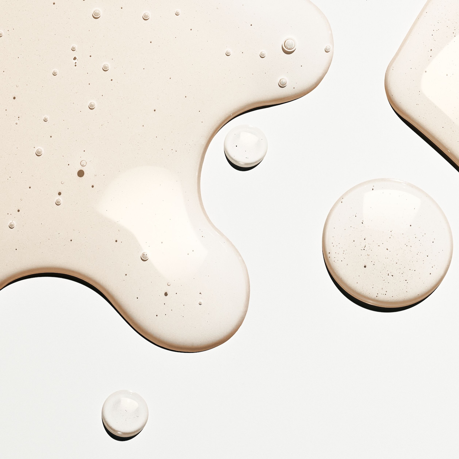 Ecco delle chiazze di siero trasparente e leggermente beige, con piccole bolle, su una superficie bianca.