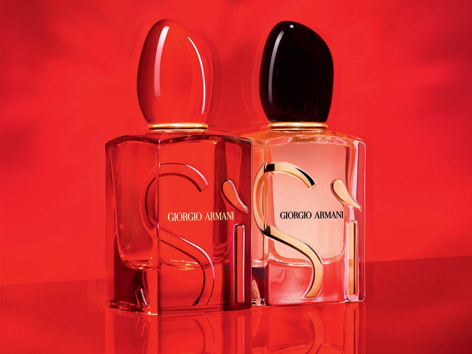 Dva flakóny vône Giorgio Armani Si, jeden s červeným vrchnákom a červenou tekutinou, druhý s čiernym vrchnákom a ružovou tekutinou, oba s logom Si v zlatej farbe.