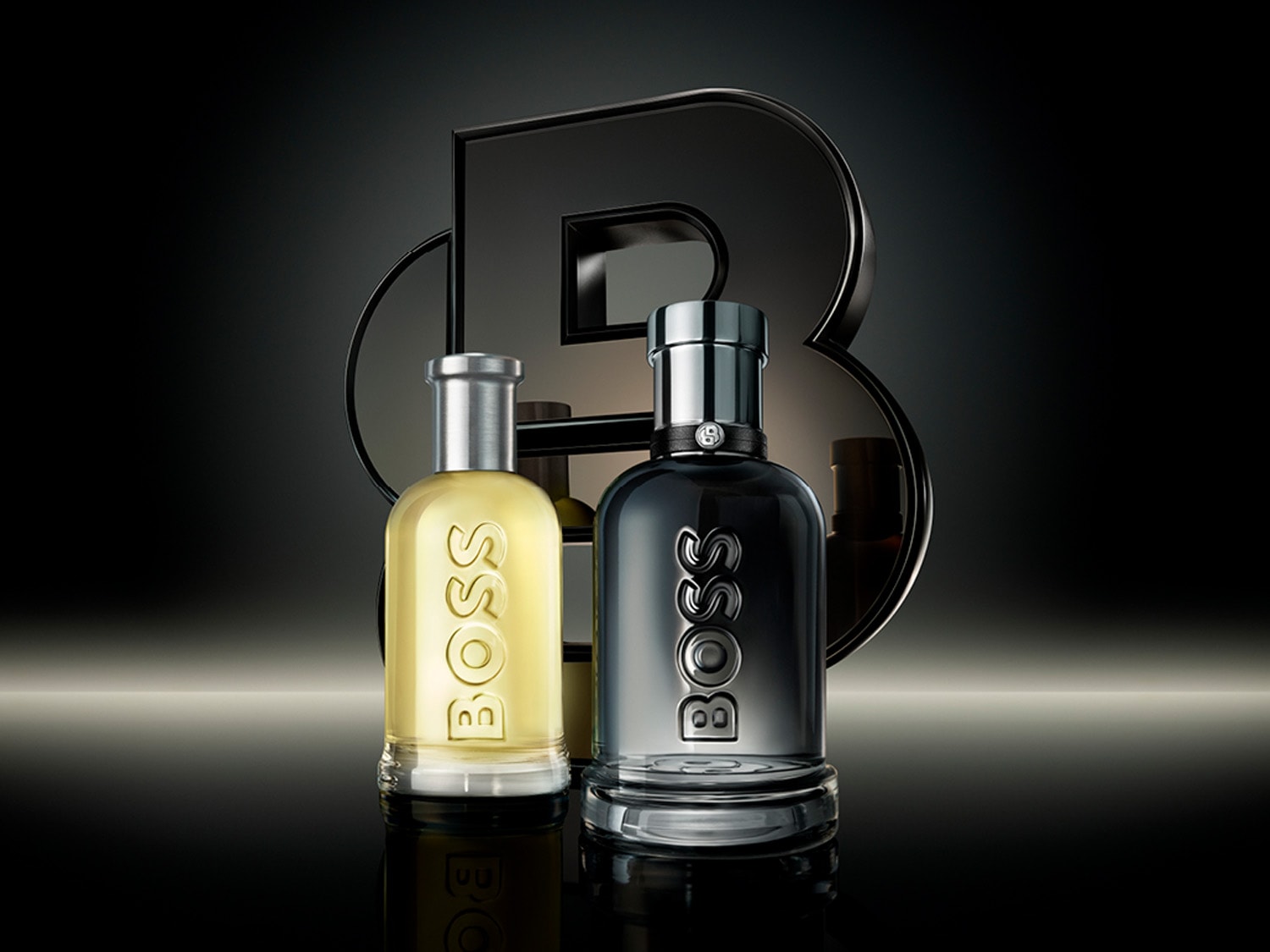 Dva flakóny vôní BOSS, jeden so svetložltou tekutinou a strieborným vrchnákom, druhý s tmavou tekutinou a tmavým vrchnákom, stoja vedľa seba pred veľkým čiernym logom BOSS.