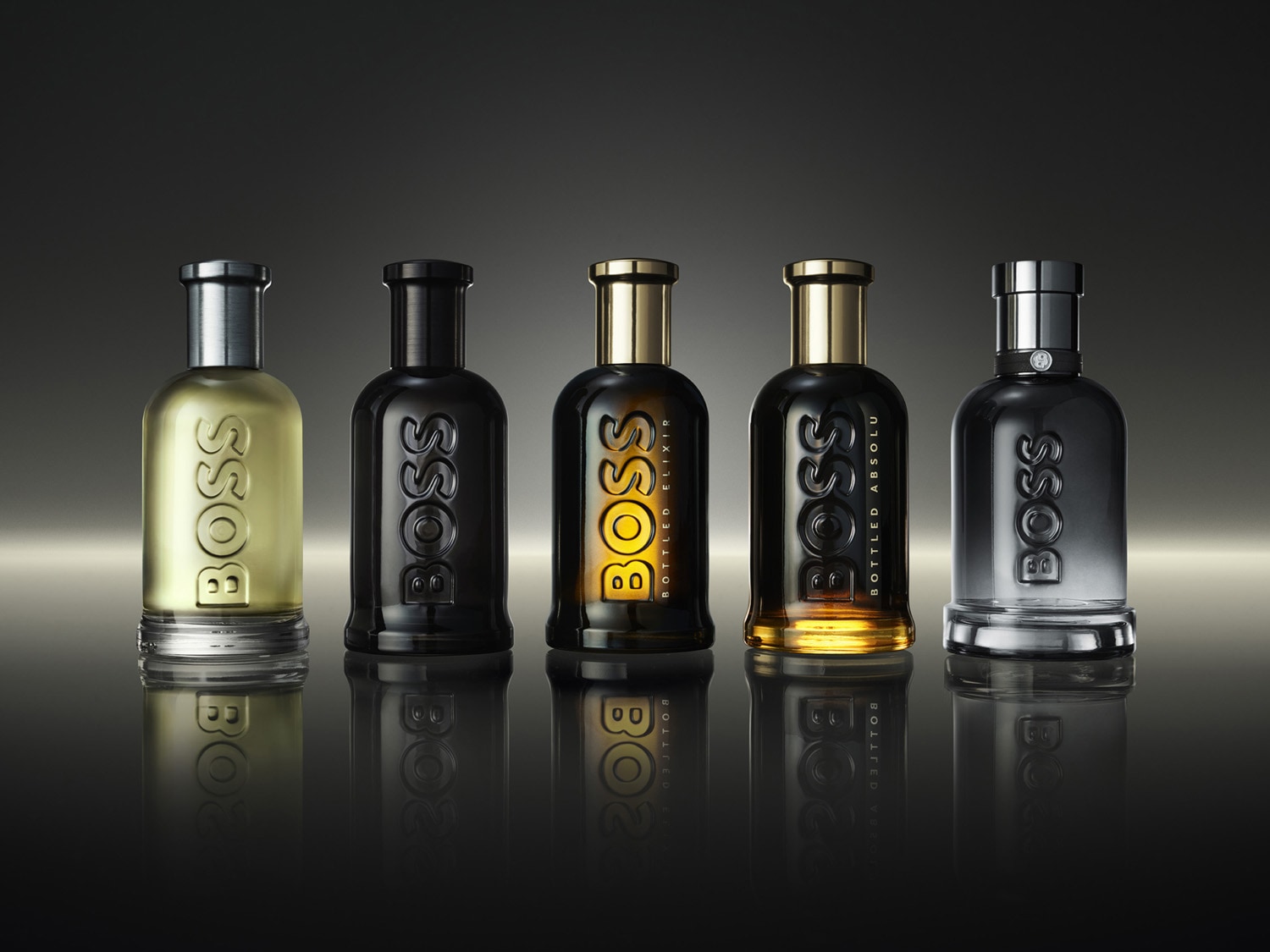 Tri čierne flakóny vôní BOSS Bottled Absolu a Elixir so zlatými viečkami stoja na kúsku dreva, čím vytvárajú luxusný a sofistikovaný dojem.