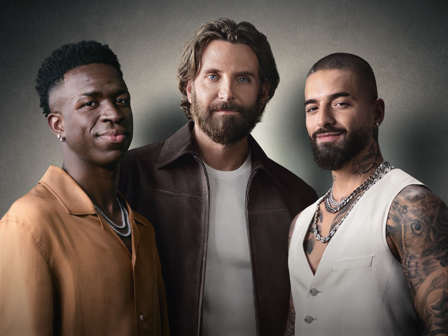 Traja muži, Vinícius Júnior, Bradley Cooper a Maluma, pózujú vedľa seba, všetci s úsmevom a štýlovým oblečením.