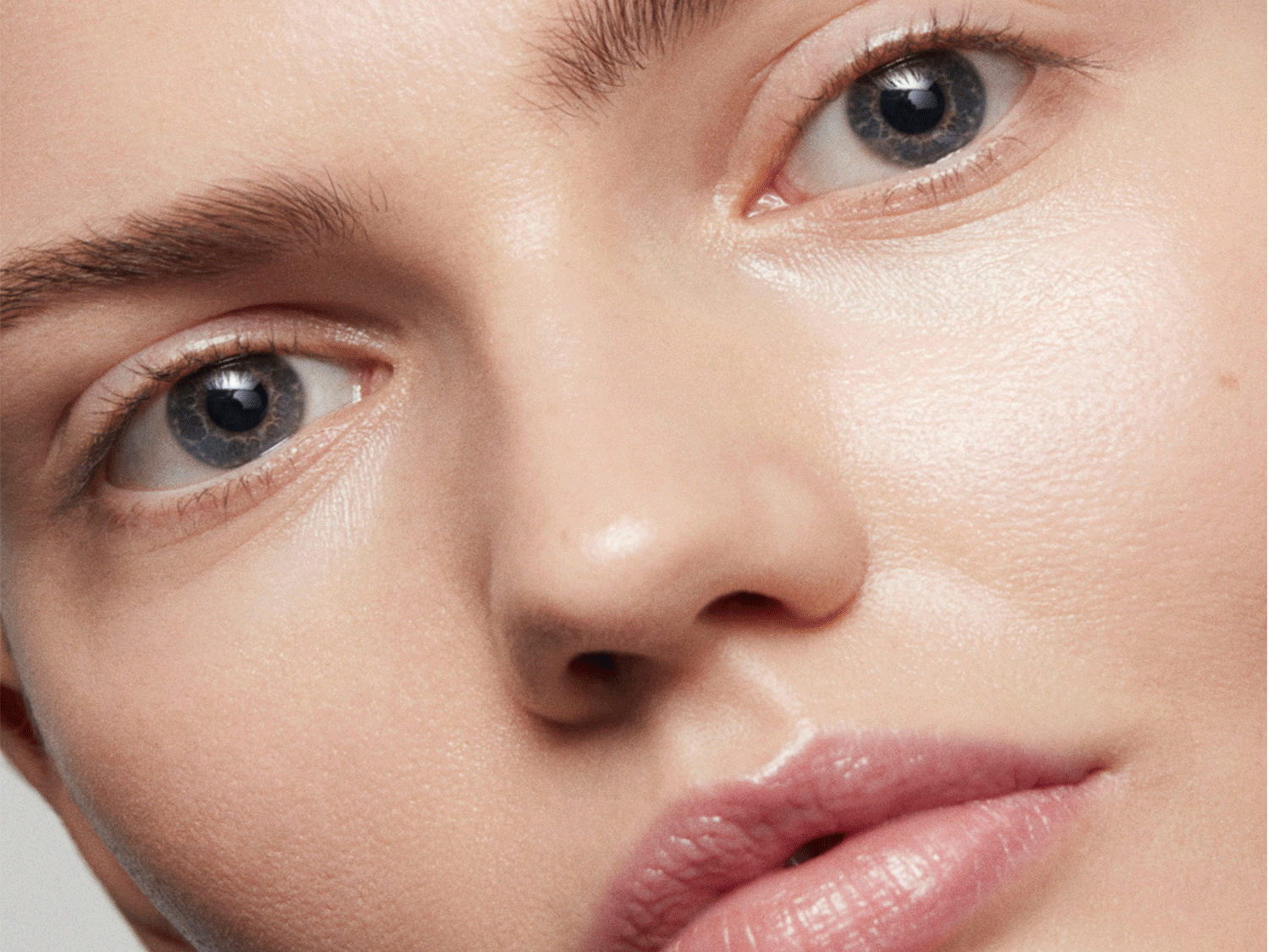 Gros plan sur le visage d'une femme à la peau claire, mettant en évidence ses yeux bleus perçants, ses sourcils bien définis et ses lèvres brillantes.