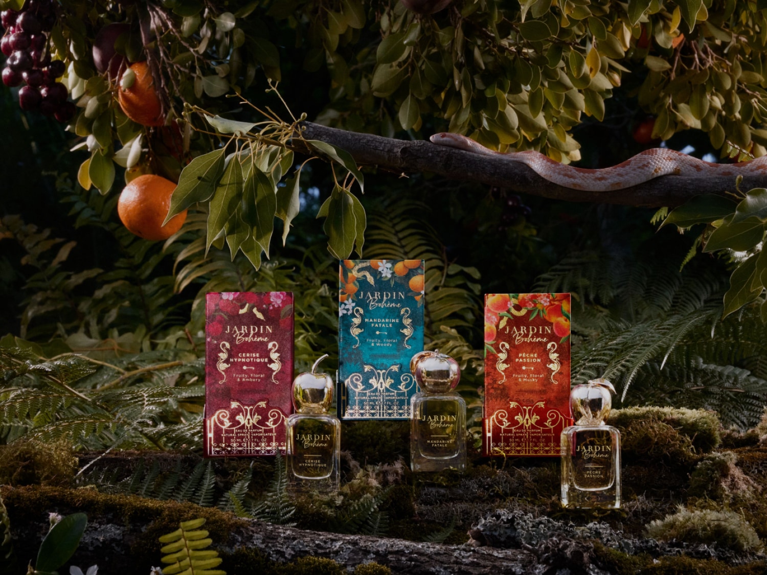 Drei Jardin Bohème Parfums stehen vor üppigem Grün, Cerise Hypnotique mit fruchtig-floralem Amberduft, Mandarine Fatale und Pêche Passion mit fruchtig-floralem Moschus.