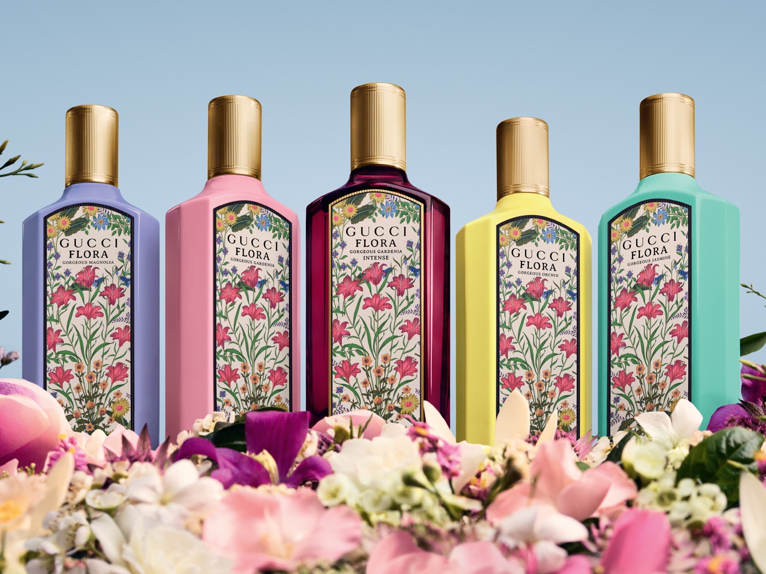 Pětice flakonů Gucci Flora v pastelových barvách, zdobených květinovými motivy a zlatými uzávěry, se tyčí nad záplavou květů.