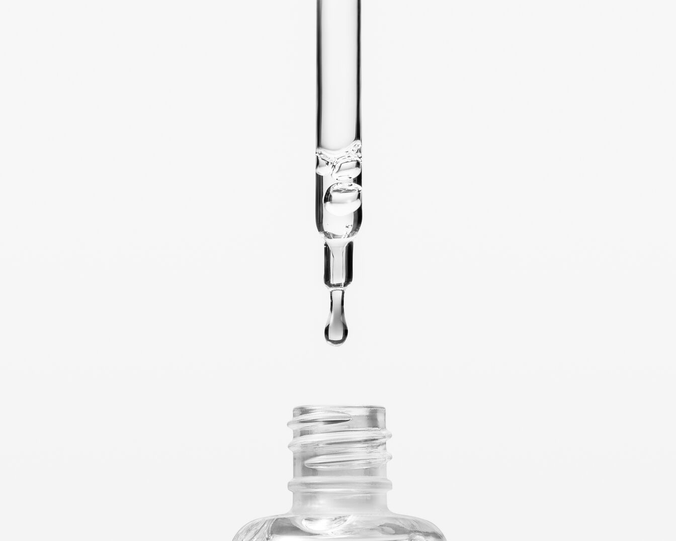 Un primo piano di un contagocce trasparente che rilascia una goccia di siero in un flacone di vetro, ideale per illustrare la purezza e l'efficacia di un prodotto di bellezza.