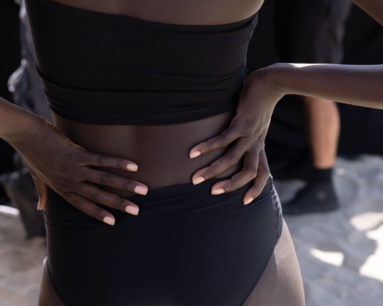 Kobieta w czarnym stroju kąpielowym trzyma ręce na biodrach, prezentując swoją sylwetkę.