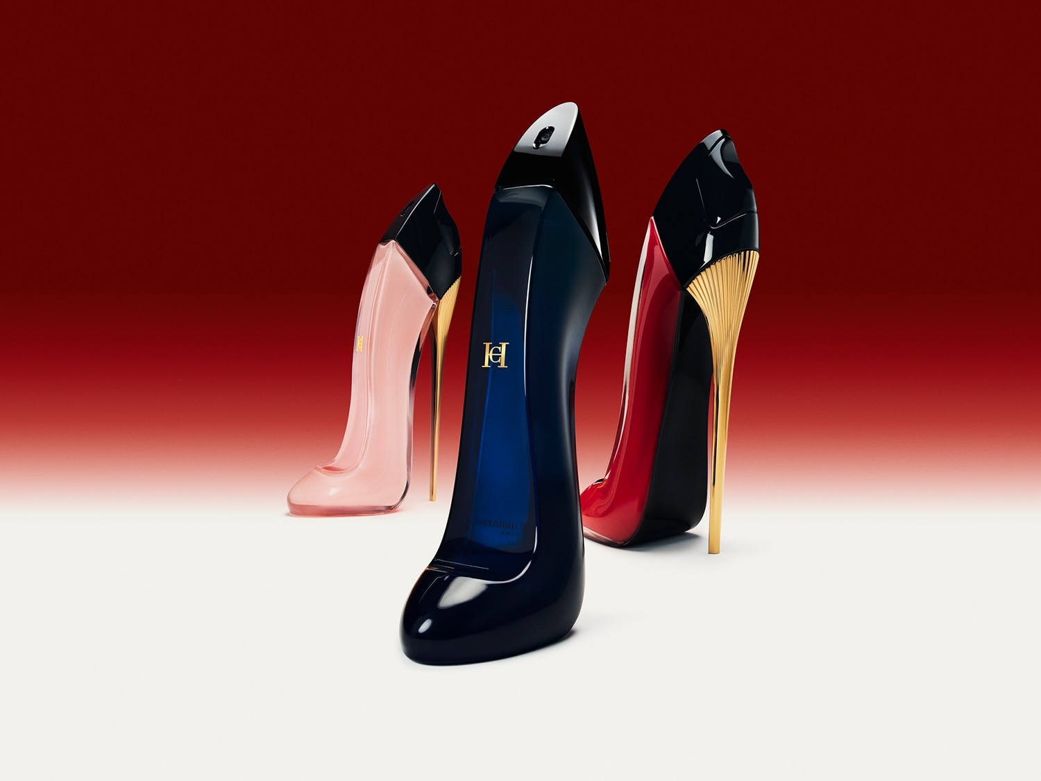 Tři flakony parfému ve tvaru dámských lodiček na vysokém podpatku v odstínech růžové, modré a červené s detaily ve zlaté barvě.