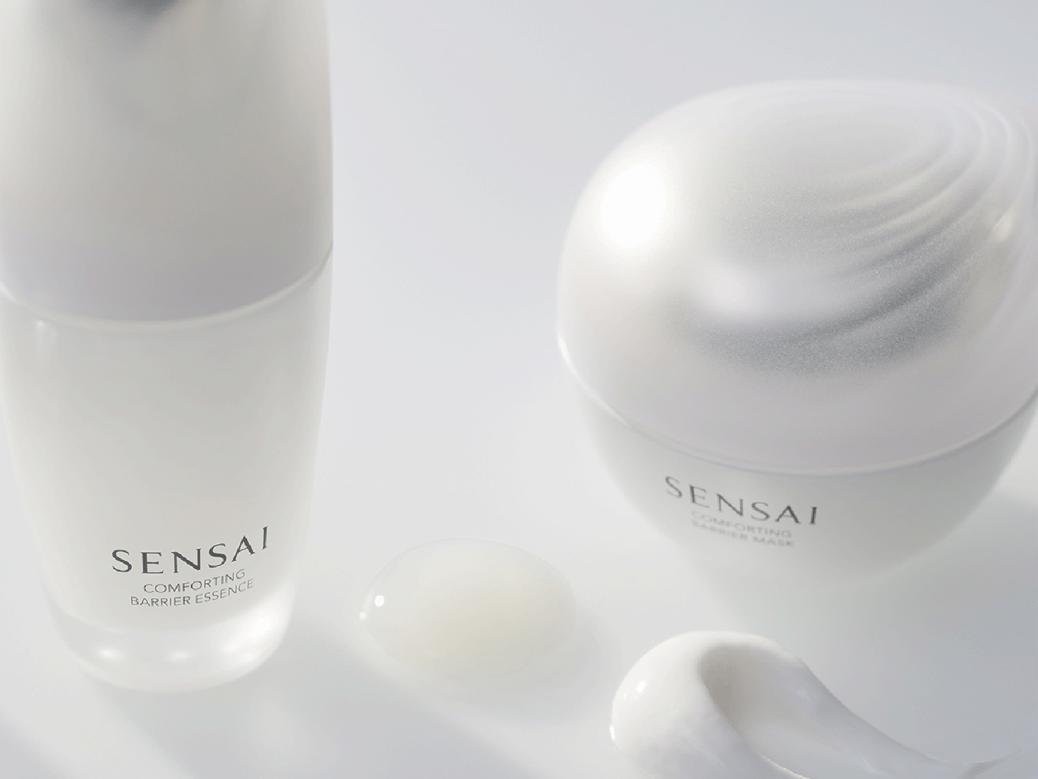 SENSAI Comforting Barrier Essence v mléčné skleněné lahvičce a maska ve vejčité nádobce, obojí s texturou pro zklidnění a ochranu pleti.