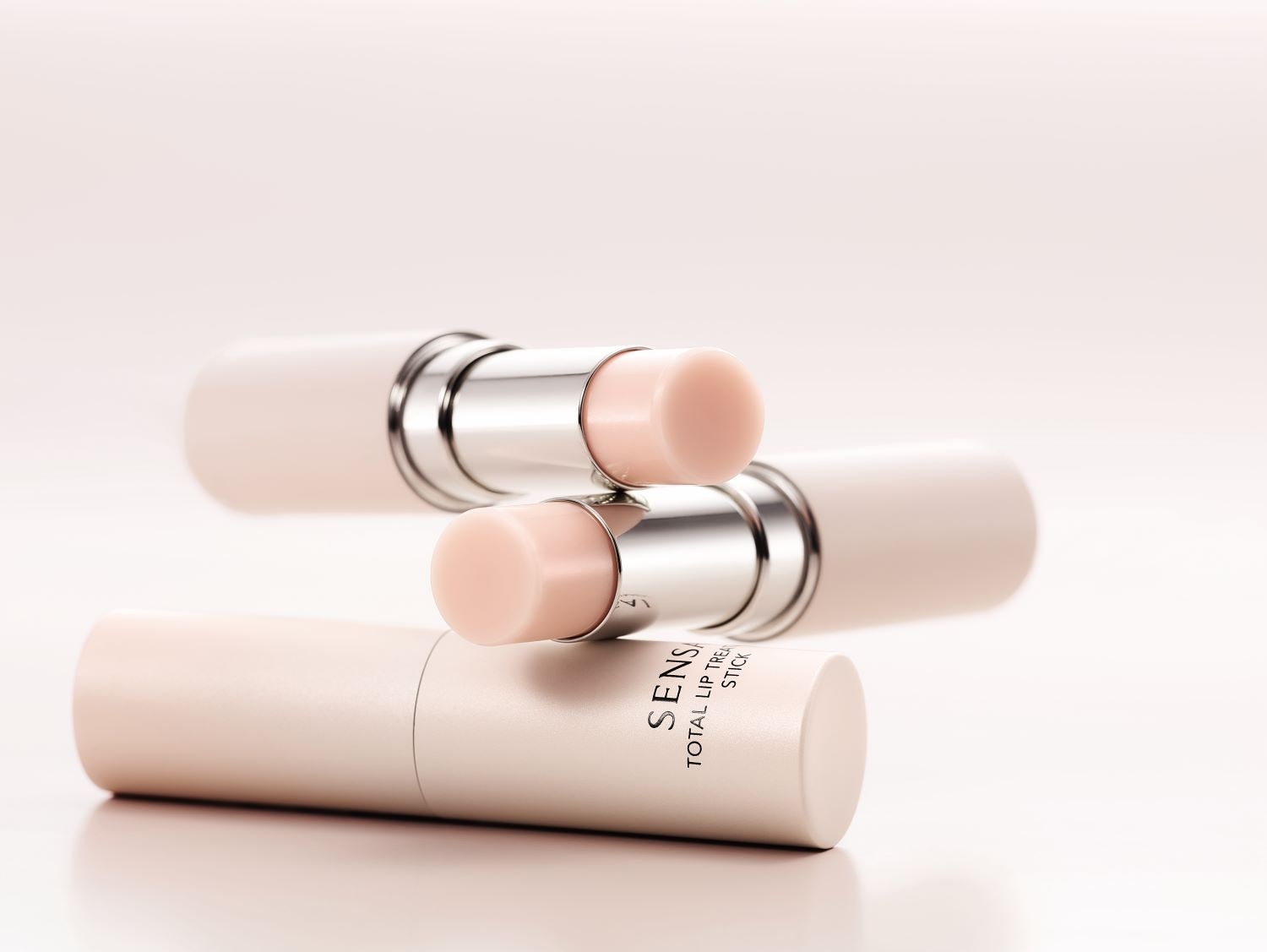 Tři balzámy na rty Sensai Total Lip Treatment Stick v béžovém obalu se stříbrnými detaily, které slibují dokonalou péči o vaše rty.
