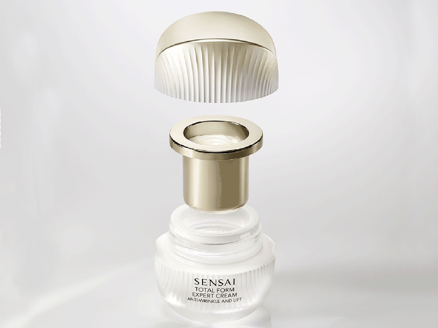 Detailní pohled na rozložený krém Sensai Total Form Expert Cream v průhledném kelímku s odhaleným zlatavým vnitřkem a víčkem, který slibuje boj proti vráskám a lifting.
