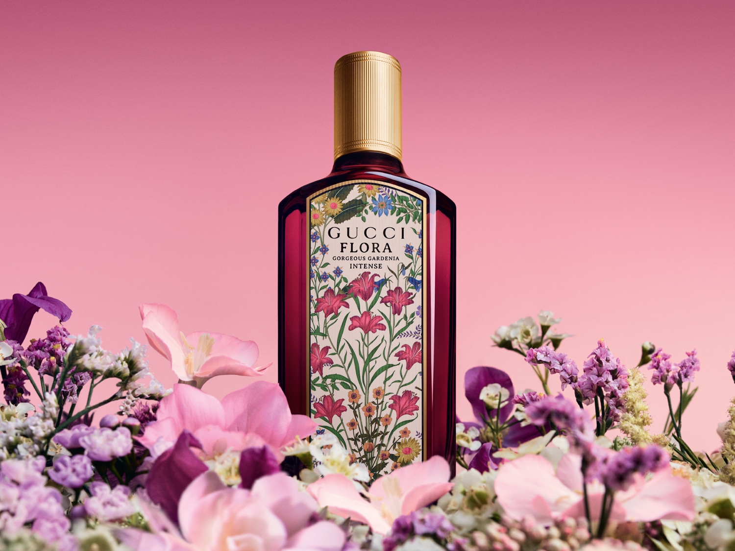 Na ružovom pozadí sa nachádza fľaša parfému Gucci Flora Gorgeous Gardenia Intense s kvetinovým vzorom, obklopená kvetmi.