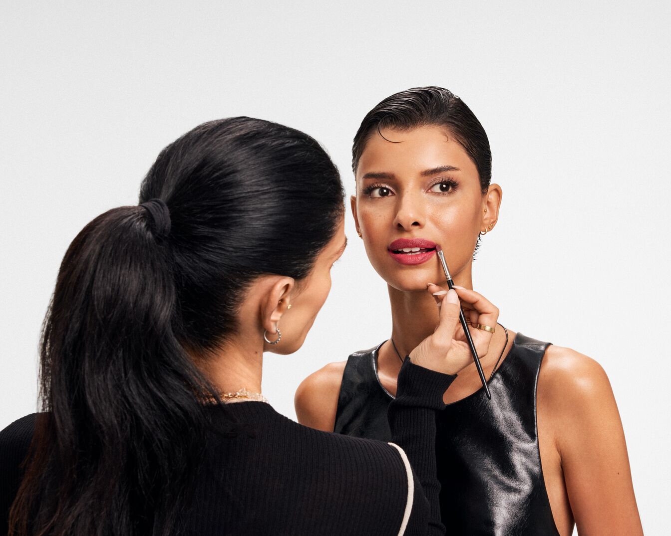 Eine Visagistin trägt mit einem Pinsel Lippenstift auf die Lippen eines Models auf, um den Look zu vervollständigen.