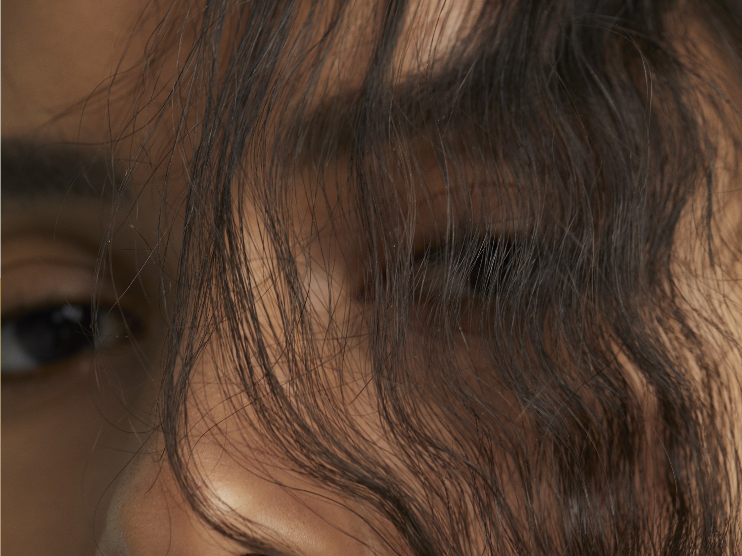 Nahaufnahme eines Gesichts mit dunklen, gewellten Haaren, die teilweise das Auge verdecken.