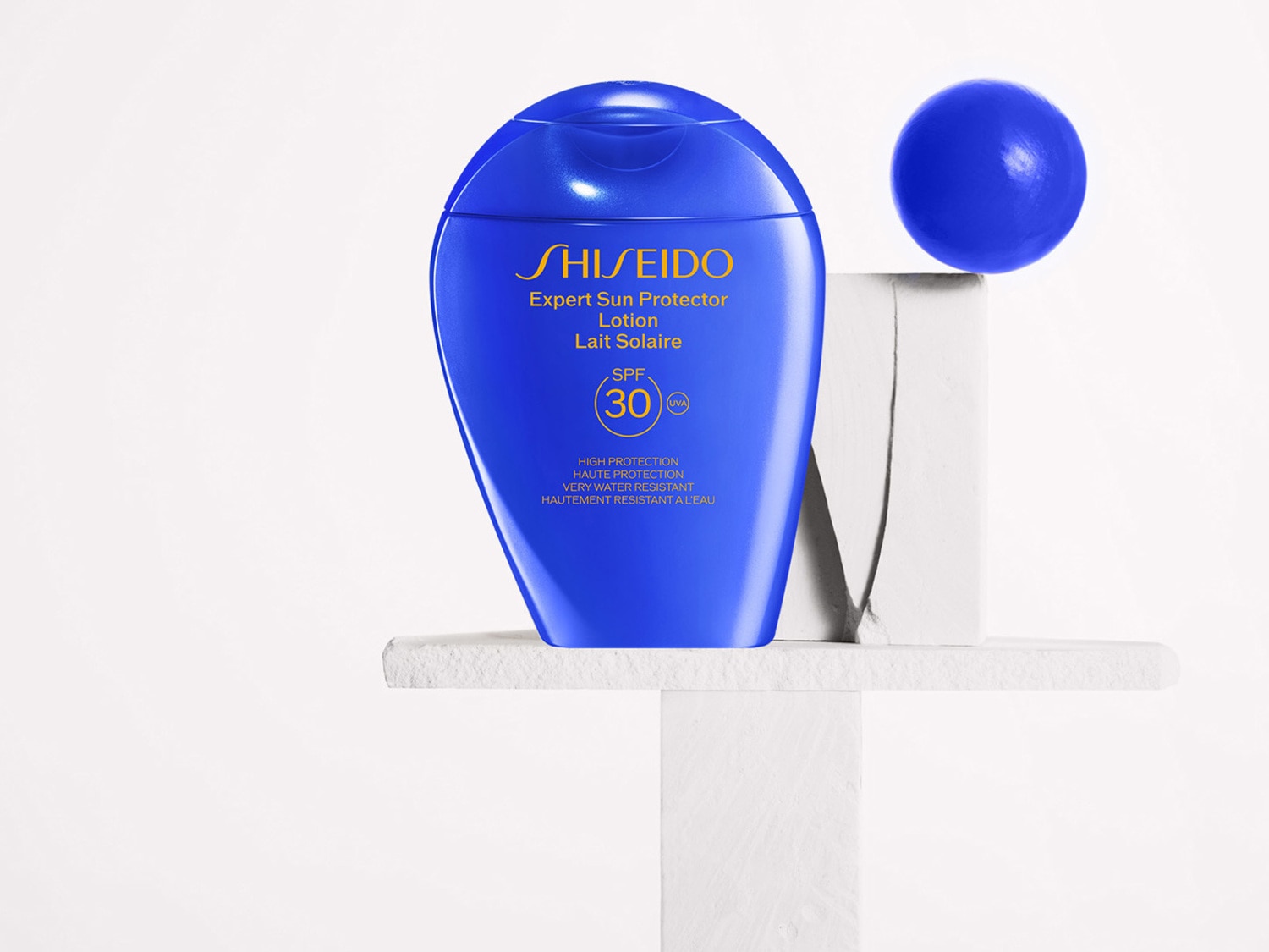 Blauwe fles Shiseido Expert Sun Protector Lotion SPF 30, die hoge bescherming biedt en zeer waterbestendig is, staat op een witte sokkel.