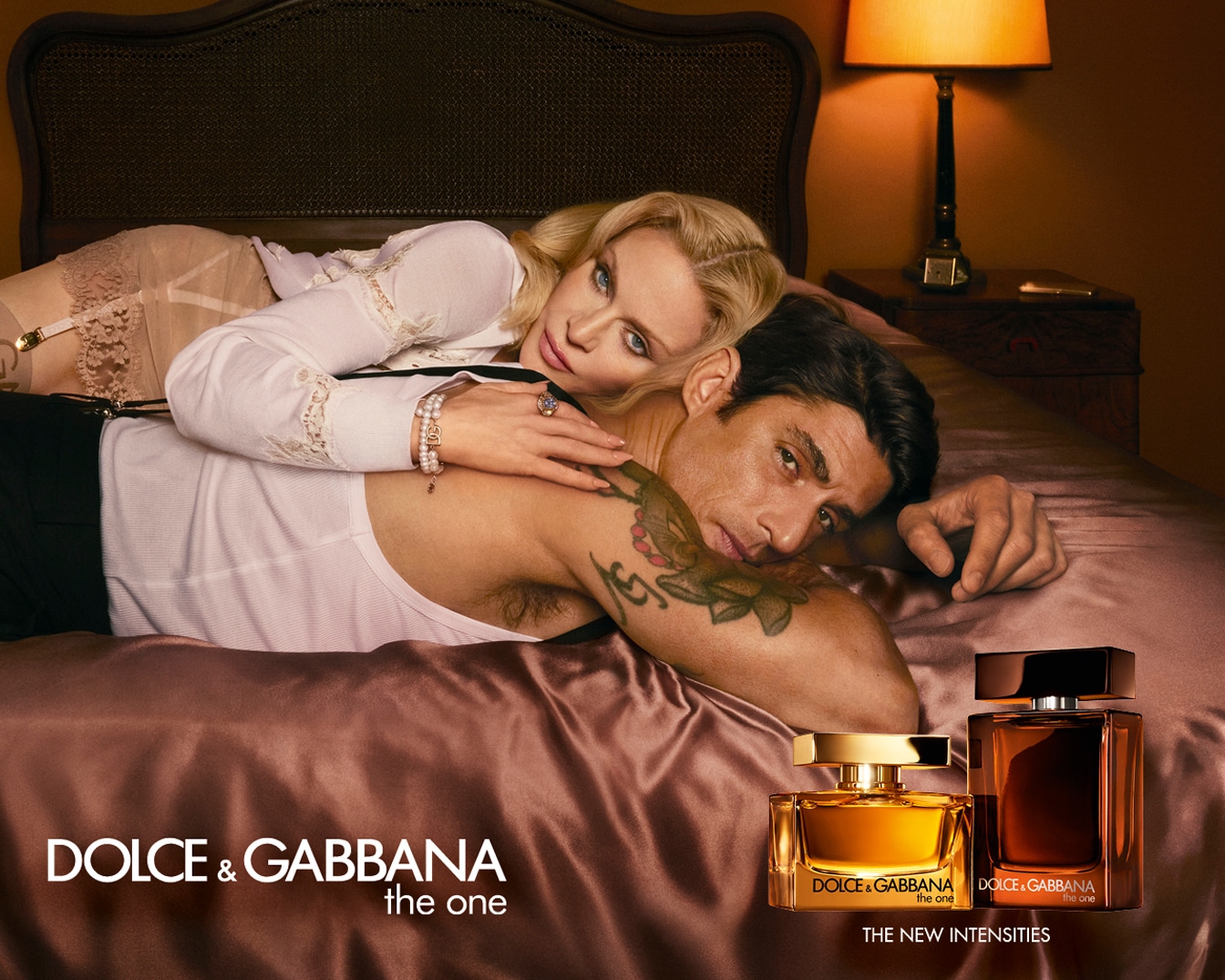 En la imagen, una pareja en la cama con los perfumes The One de Dolce & Gabbana, uno dorado y otro marrón, resaltando 'The New Intensities'.