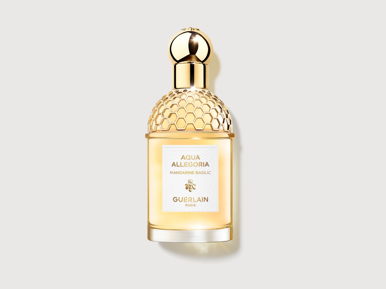 El frasco de perfume Aqua Allegoria Mandarine Basilic de Guerlain, con un tapón dorado y un diseño de panal, evoca una fragancia cítrica y fresca.