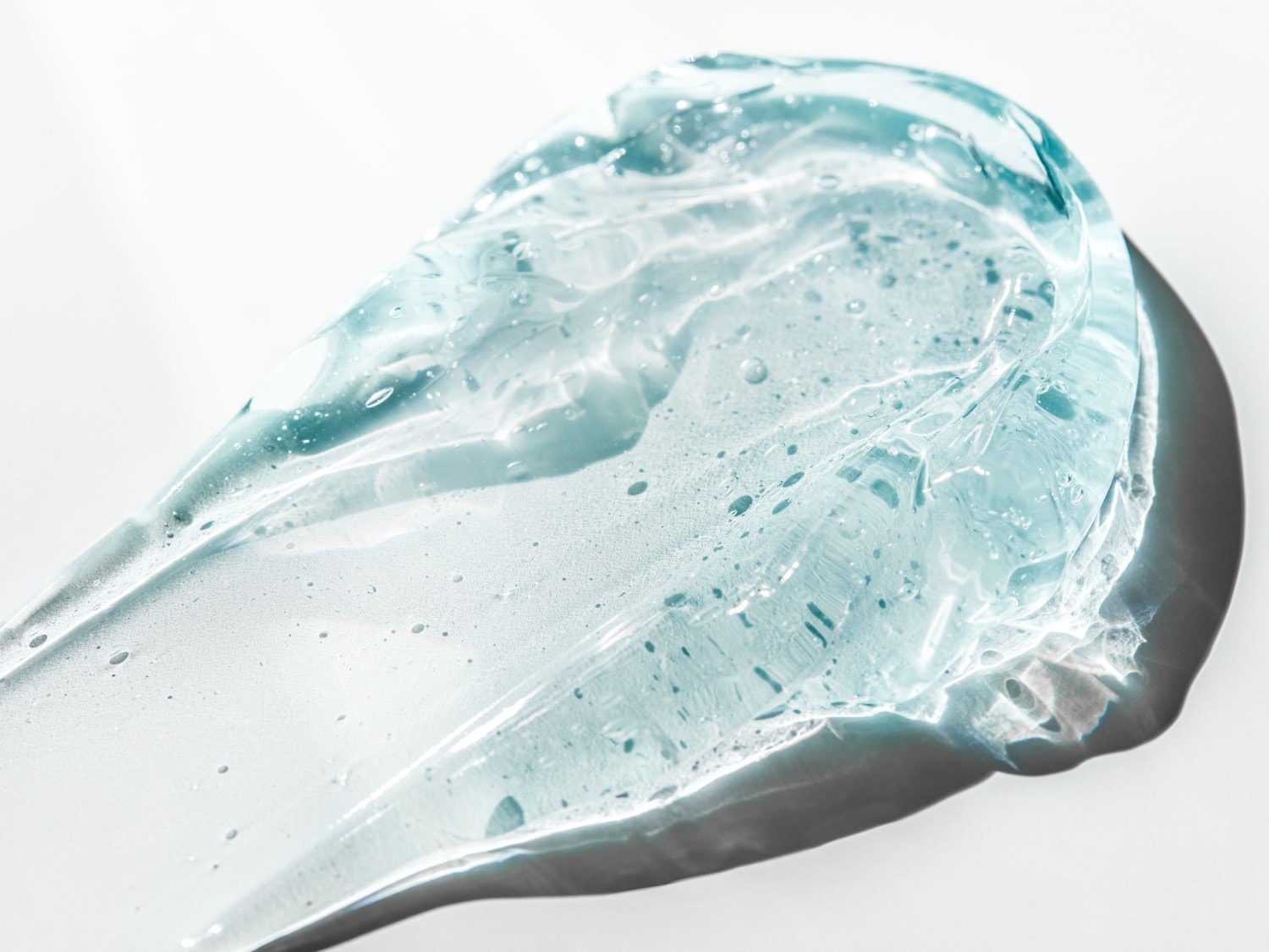 Close-up van een heldere, lichtblauwe gel met kleine luchtbelletjes, uitgespreid op een witte achtergrond, die de textuur en consistentie van het product laat zien.