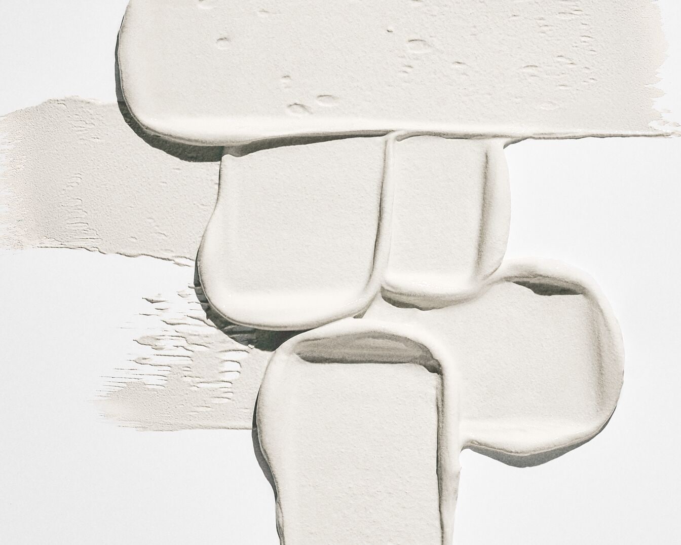 Dichte, crèmekleurige cosmetische vegen in verschillende texturen liggen op een witte achtergrond.