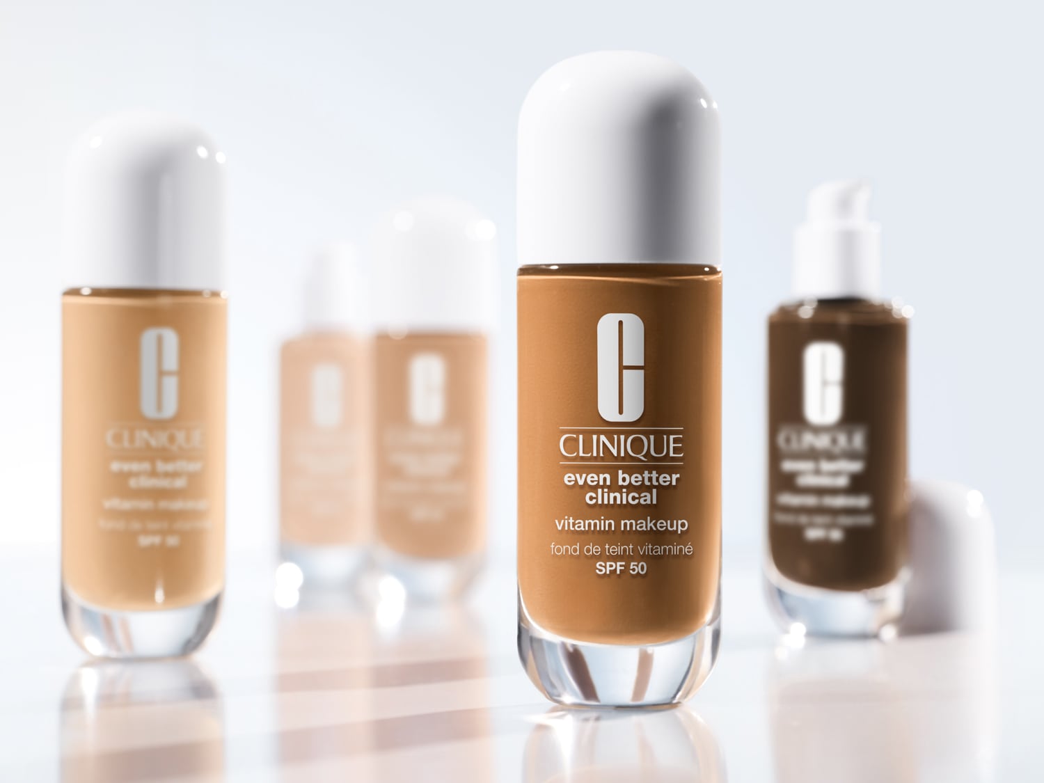 Clinique Even Better Clinical Vitamin Makeup SPF 50 v rôznych odtieňoch, balené v priehľadných sklenených fľaštičkách s bielym vrchnákom, sľubujúce dokonalé krytie a ochranu pleti.