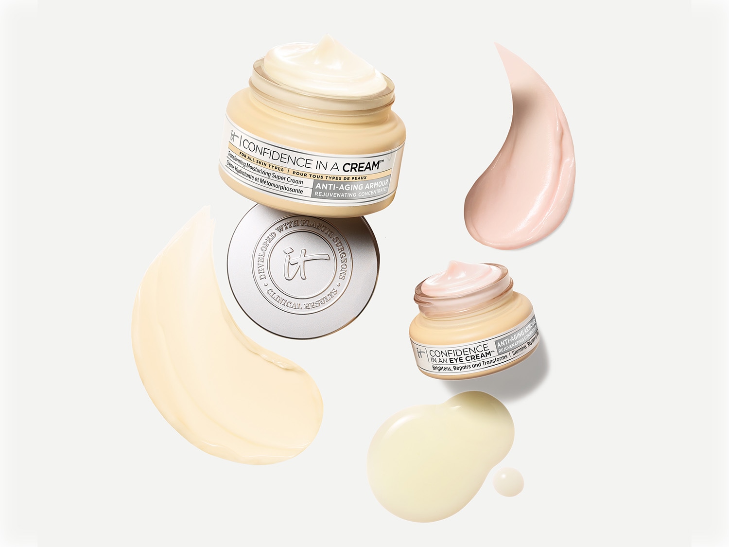 Krem i krem pod oczy IT Cosmetics Confidence w beżowych słoiczkach z srebrnymi nakrętkami, obok których znajdują się próbki kremu o różnych odcieniach.