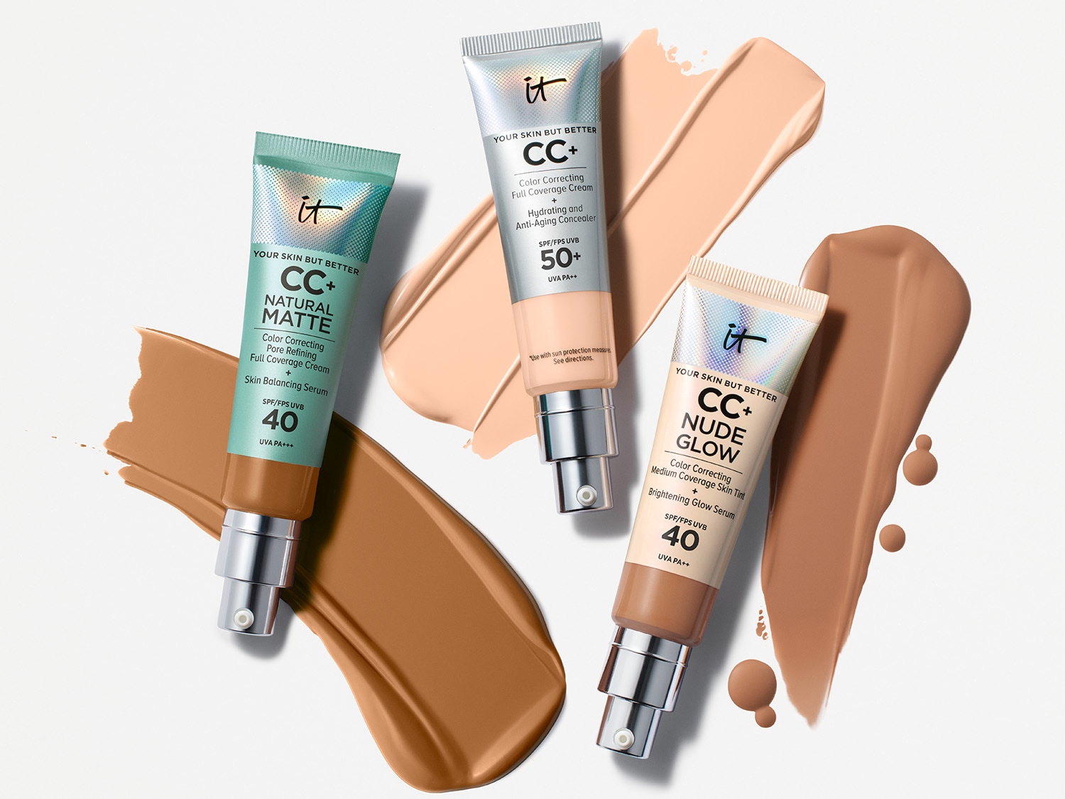 Trzy tubki kremu CC+ marki IT Cosmetics w odcieniach Natural Matte, Nude Glow i Full Coverage Cream, każdy z pompką i SPF, obok smug odpowiadających kolorów.