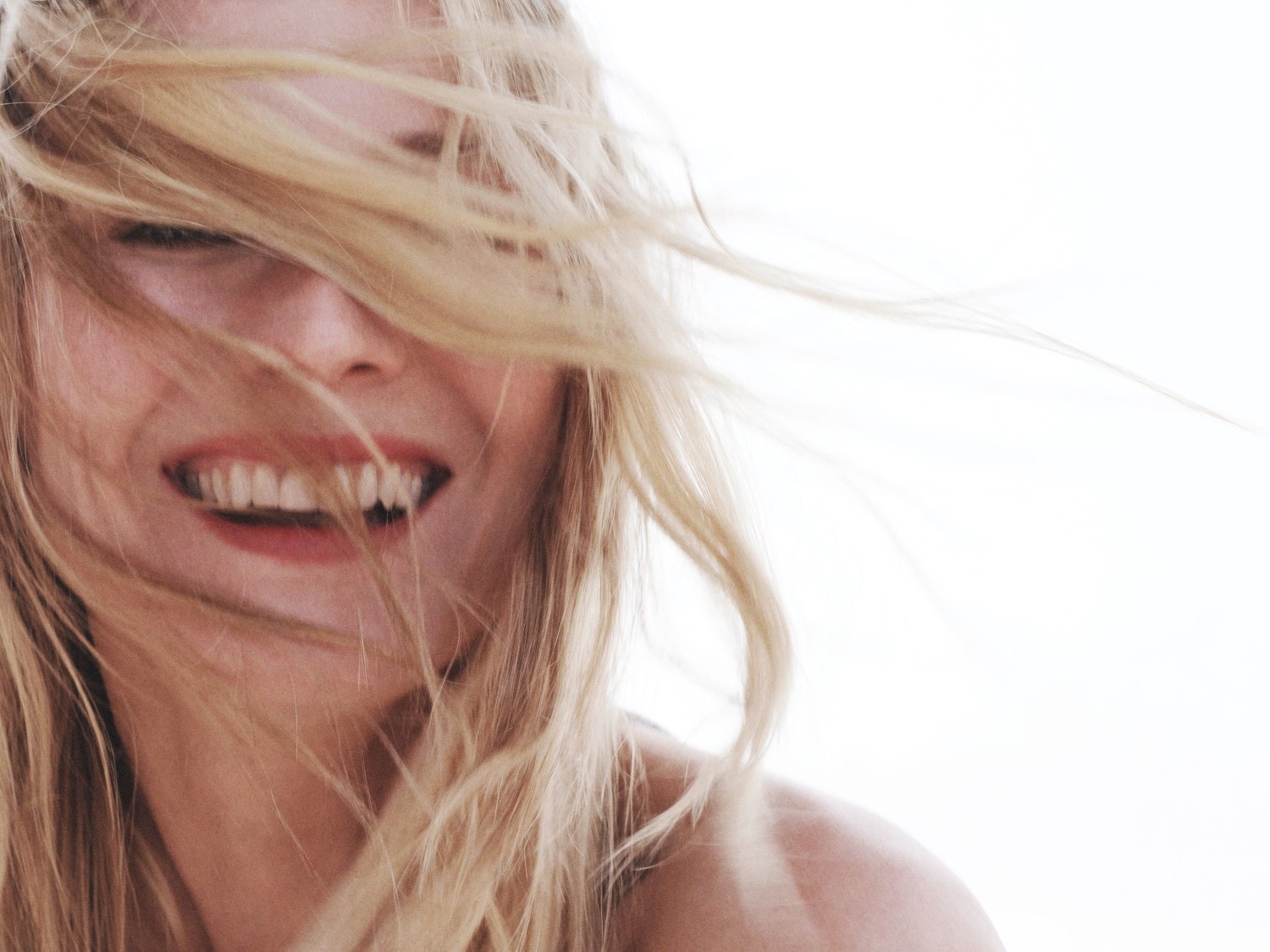 Nahaufnahme einer lächelnden Frau mit blonden Haaren, die ihr Gesicht umspielen.