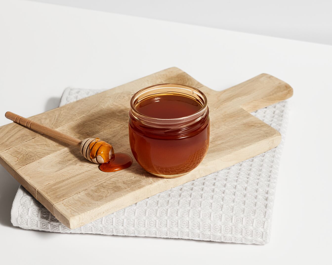 Ein Glas goldener Honig steht auf einem Holztisch neben einem Honiglöffel, der ebenfalls mit Honig bedeckt ist.