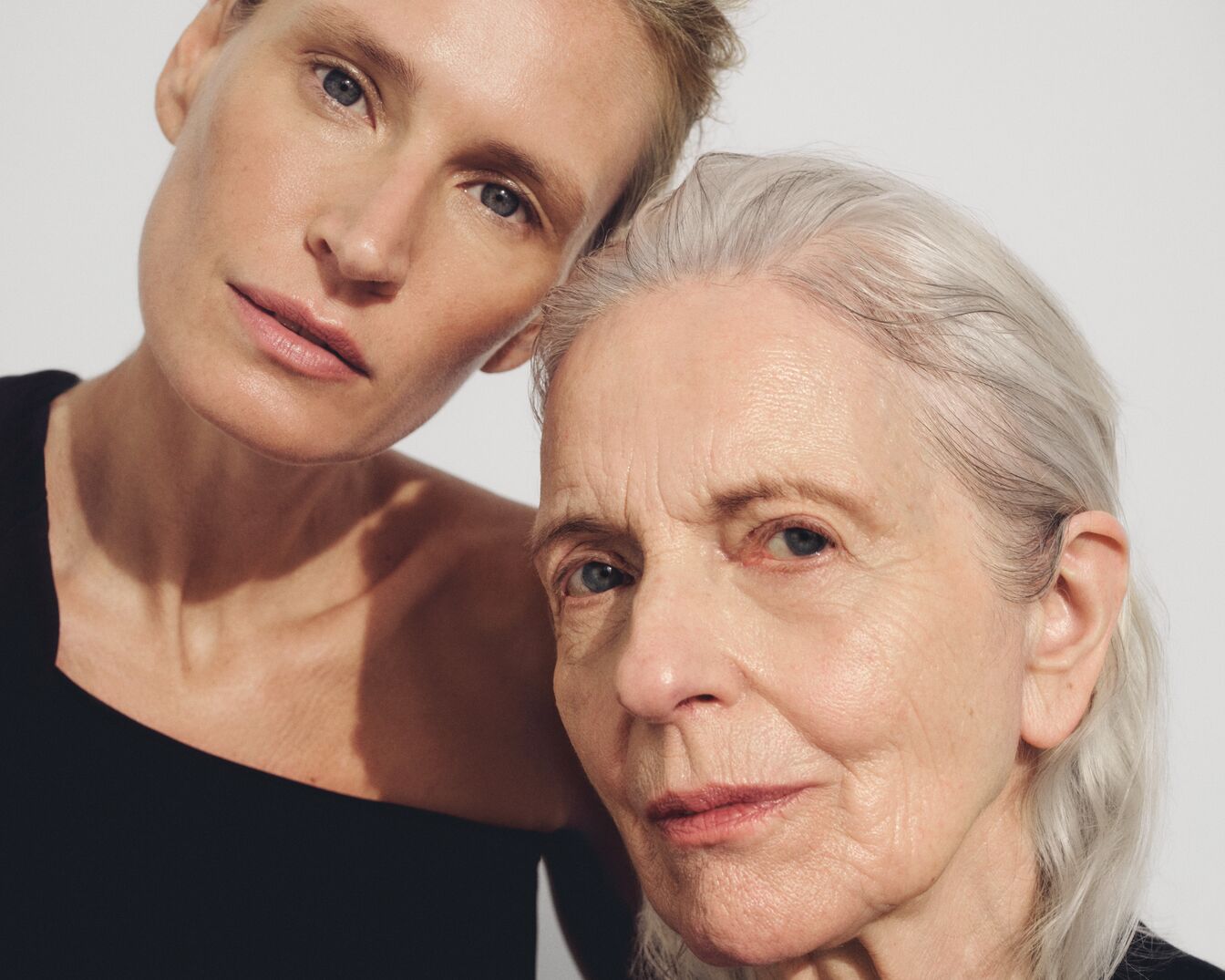 Nahaufnahme von zwei Frauen unterschiedlichen Alters, die ihre Wangen aneinanderlegen und einen natürlichen Hautton zeigen.
