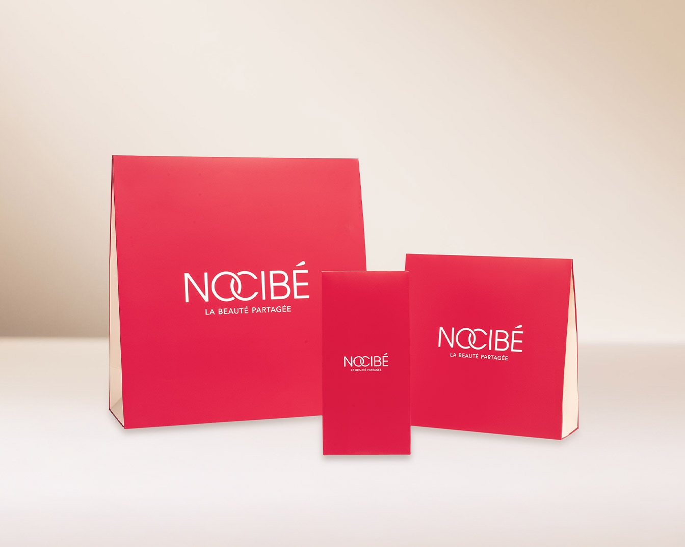 Trois boîtes rouges Nocibé de différentes tailles sont présentées, portant le logo blanc et la mention 'La Beauté Partagée'.
